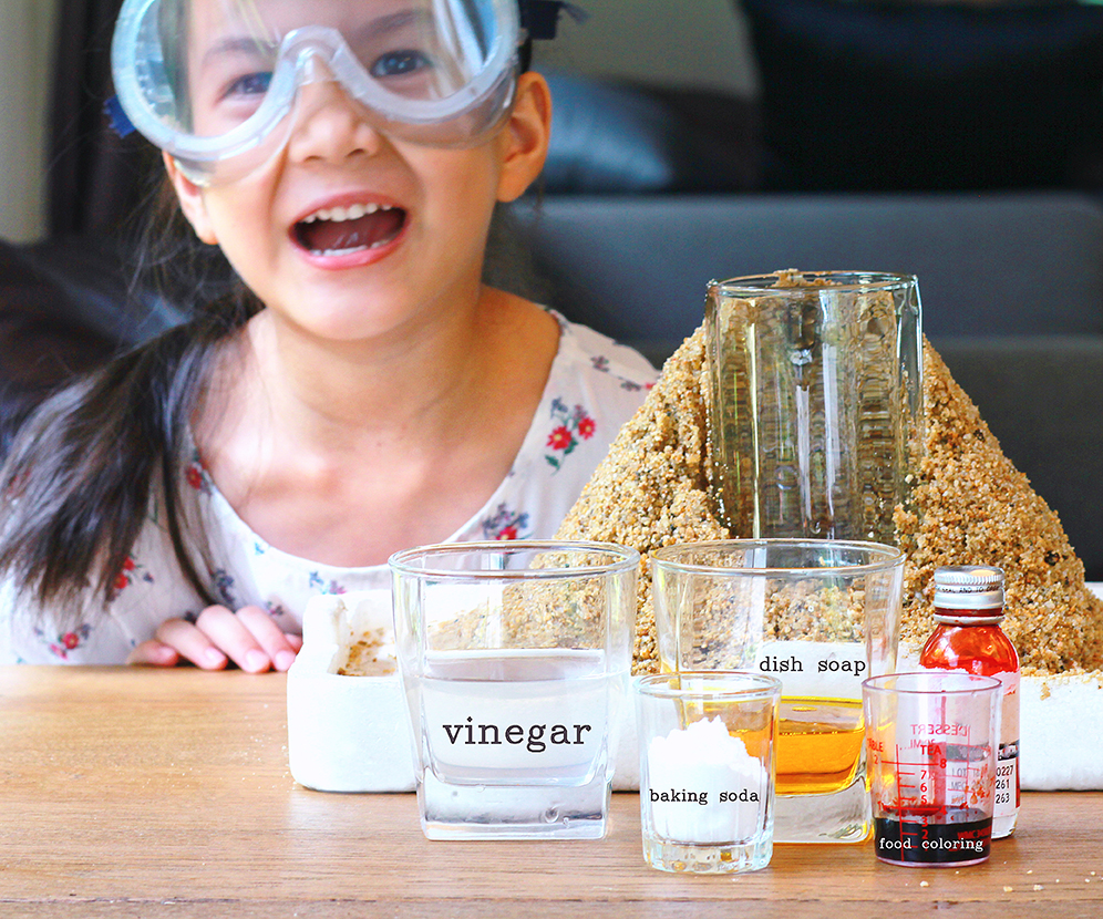 A young girl poses with the ingredients for a volcano simulation.